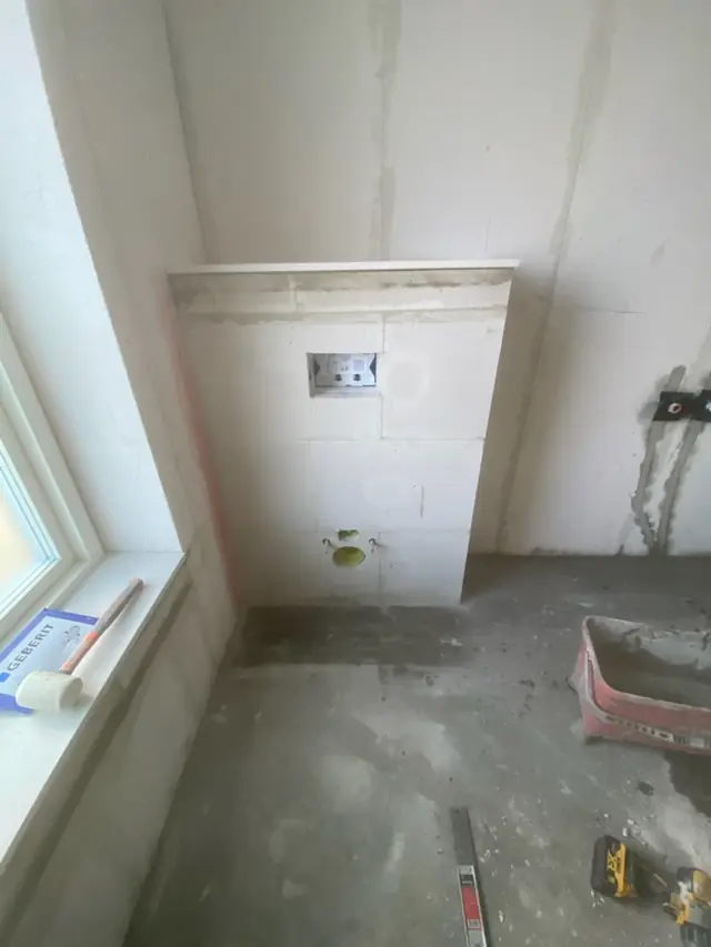 Muret installationsvæg til indbygget cisterne med tilslutninger og en gummihammer i vindueskarmen