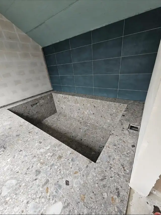 Nedsænket kar beklædt med gråt terrazzo på både gulv, sider og bund, op mod en væg af mørkeblå fliser